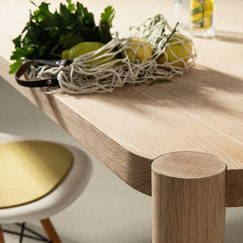 detail vom loop esstisch mit massiver tischpatte aus eichenholz und runden tischbeinen ein einkaufsnetz mit zitronen und petersilie und eames chair