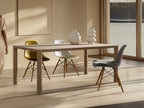 loop esstisch aus eiche massivholz in wohnzimmer mit blick auf see mit eames plastic side chairs und zwei vasen auf der tischplatte frau von hinten