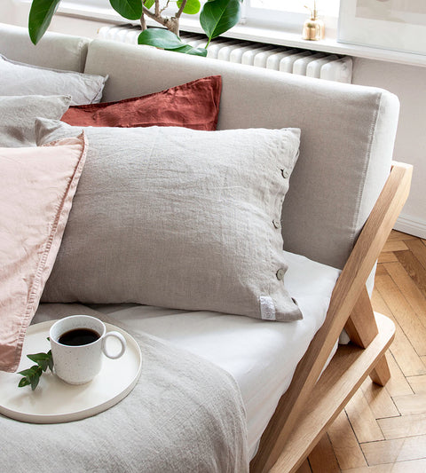 designdetail von nordic space bett mit bettgestell aus eiche massivholz polster kissen in der farbe natur und kaffeetasse auf tablett
