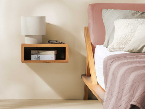 nordic space bett mit rückenpolster in herbstrosa und kissen daneben wandhängender nachtisch aus eiche massivholz mit offenem ablagefach für bücher und tischleuchte darauf