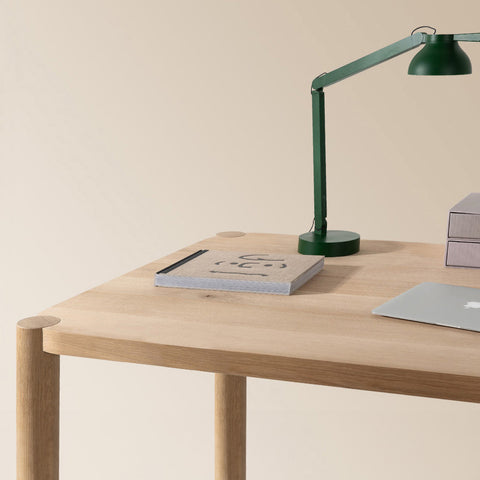 loop schreibttisch aus eiche massivholz mit runden tischbeinen und tischleuchte buch und laptop auf tischplatte
